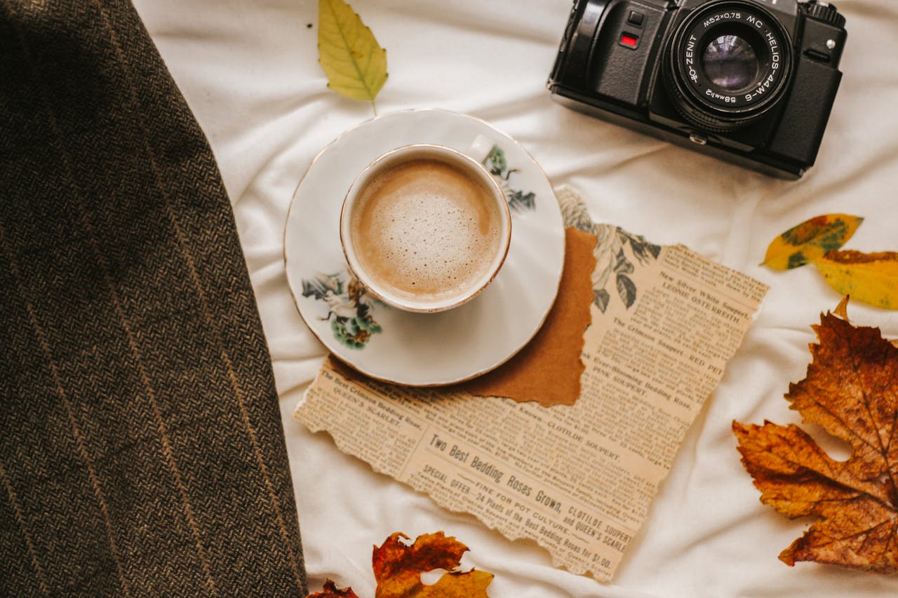 A warm autumn arrangement featuring coffee, camera, and vintage newspaper.